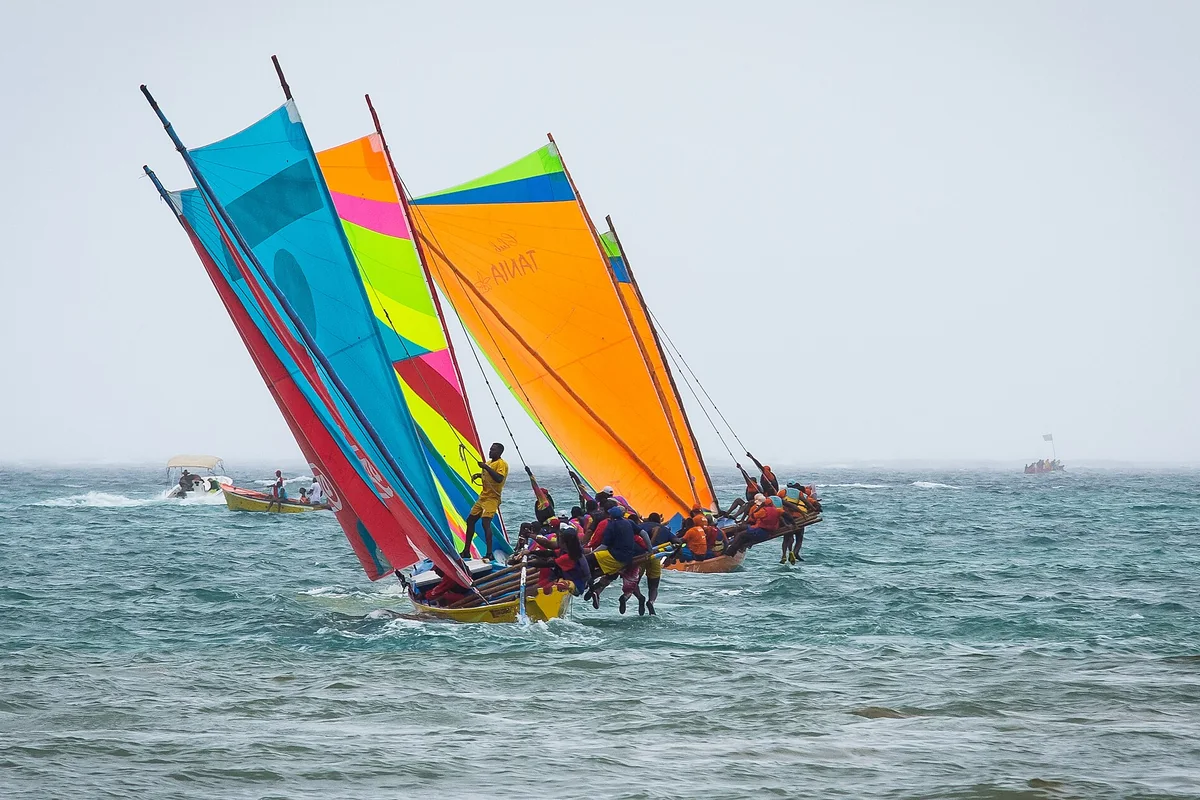 Équipages en course sur des yoles rondes aux voiles colorées en Martinique